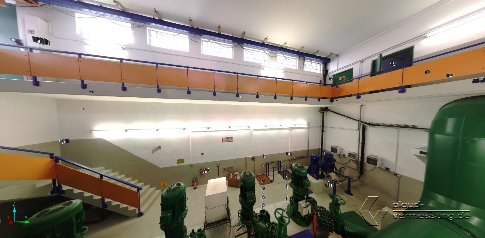 Eine weite Innenaufnahme eines Raumes mit grünen Rohren, Treppen und Industrieanlagen. Weiße Wände und orangefarbene Zierleisten.