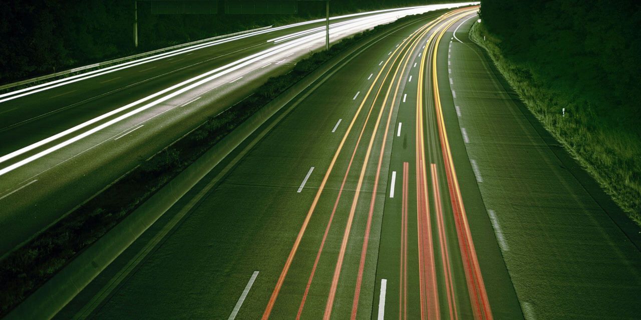 Nächtliche Autobahn mit verschwommenen Lichtstreifen von fahrenden Fahrzeugen.