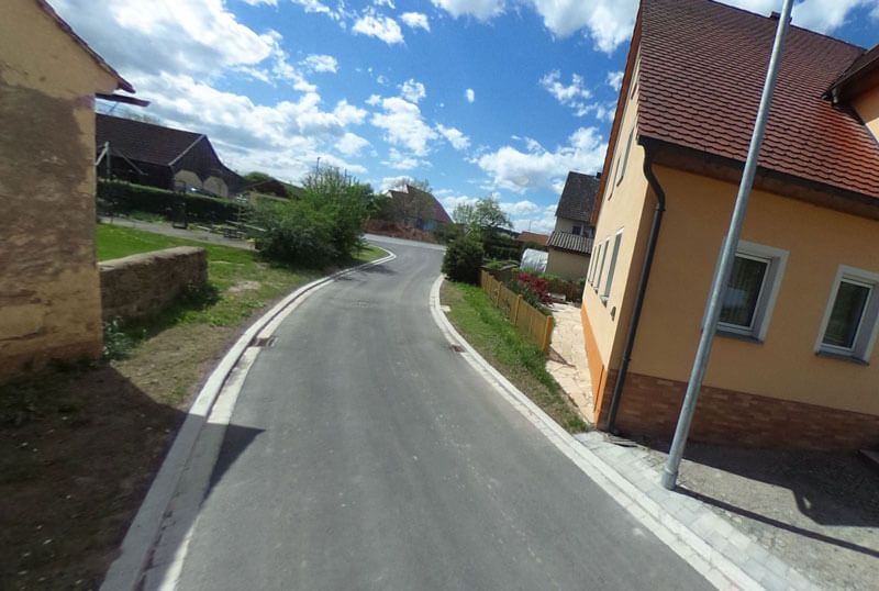 Eine kurvenreiche Straße durch eine kleine Stadt an einem sonnigen Tag, mit sichtbaren Häusern und blauem Himmel.