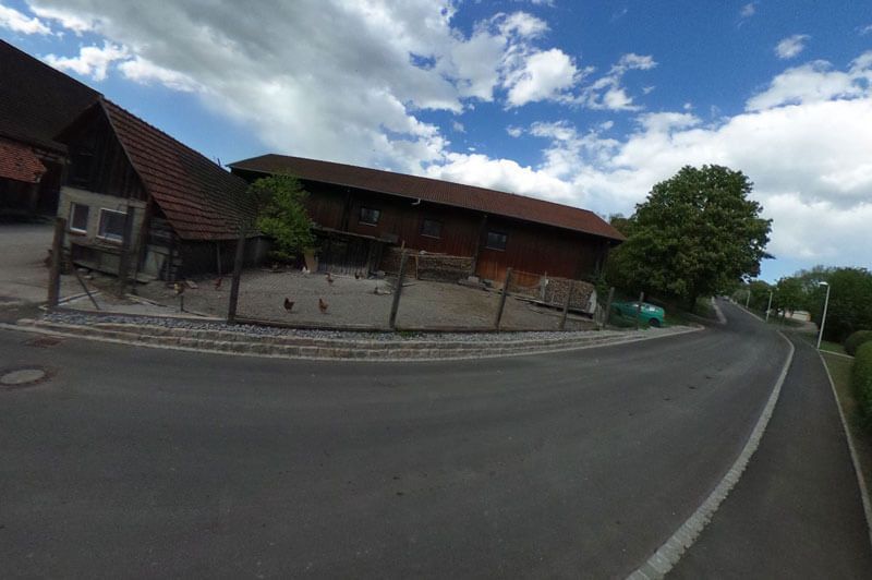 Eine Landstraße schlängelt sich unter einem wolkenlosen blauen Himmel an verwitterten Holzgebäuden vorbei.