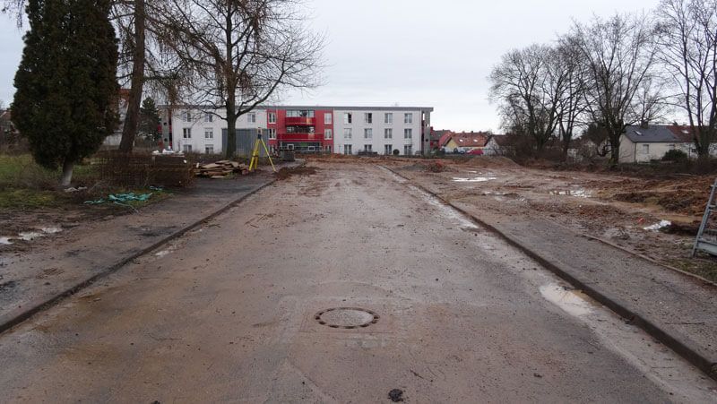 Eine schlammige Straße führt zu einem Gebäude. Bauschutt und nasser Boden. Bewölkter Tag.