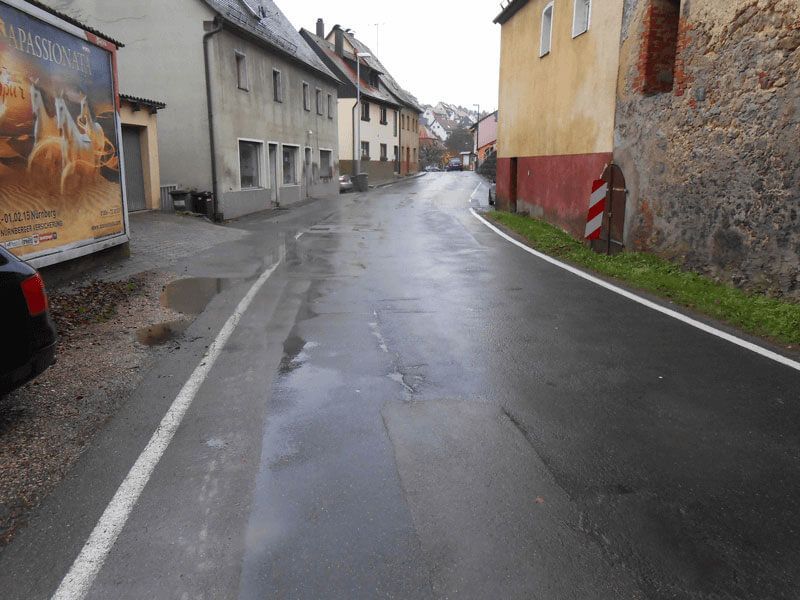 Nasse Straße in einer europäischen Stadt, gesäumt von Gebäuden und einem geparkten Auto.