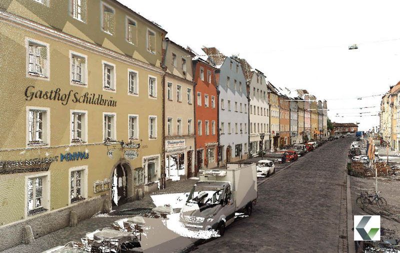 Eine Reihe farbenfroher Gebäude säumen eine Kopfsteinpflasterstraße, mit geparkten Fahrzeugen und einem Lastwagen im Vordergrund.