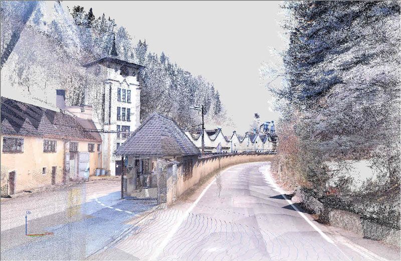 Eine Straße schlängelt sich an Gebäuden und einem bewaldeten Hügel vorbei, dargestellt im Punktwolkenstil.