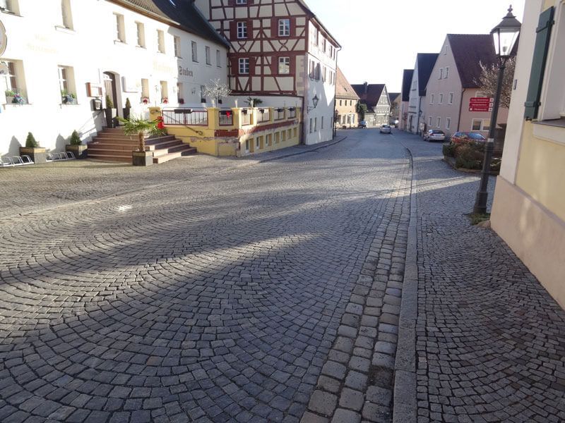 Kopfsteinpflasterstraße auf dem europäischen Stadtplatz, Gebäude mit abwechslungsreicher Architektur und Schatten.