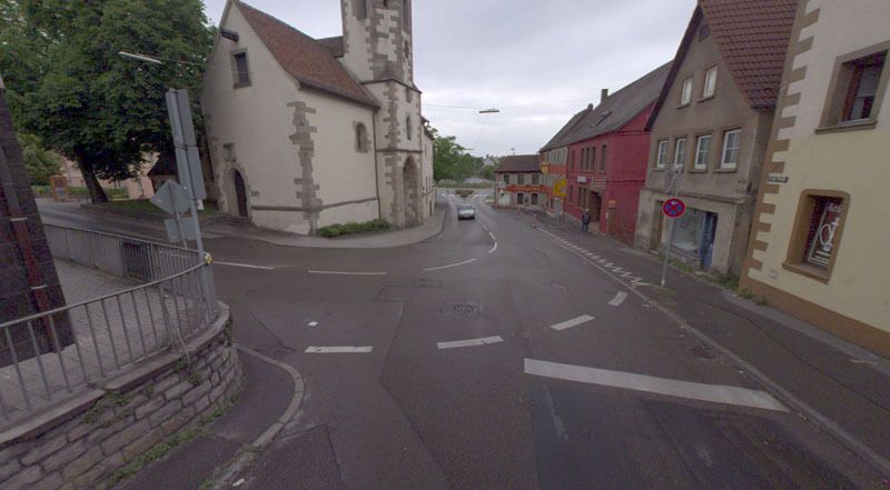 Straßenszene mit Kirche, Gebäuden und einem Auto, das auf einer nassen Straße fährt.