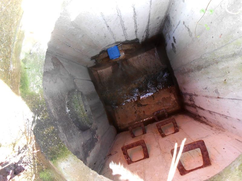 Blick in einen Betonbrunnen, der einen dunklen, quadratischen Boden mit etwas Wasser und einem blauen Quadrat zeigt.