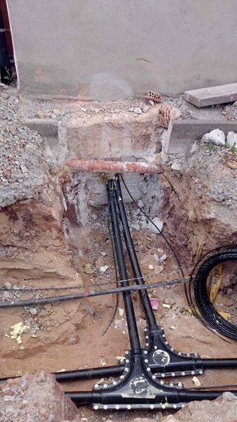 Unterirdische Stromleitungen, die aus einem Graben neben einer Betonwand herausragen.