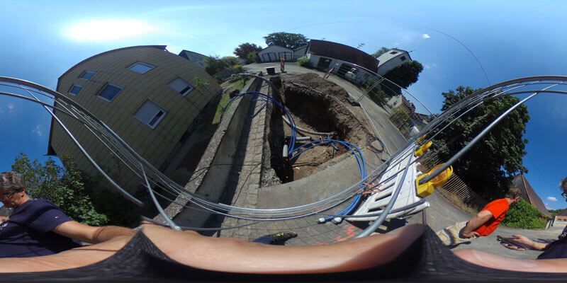 Arbeiter in der Nähe eines Grabens in einer Straße; blaue Rohre und Ausrüstung; sonniger Tag.