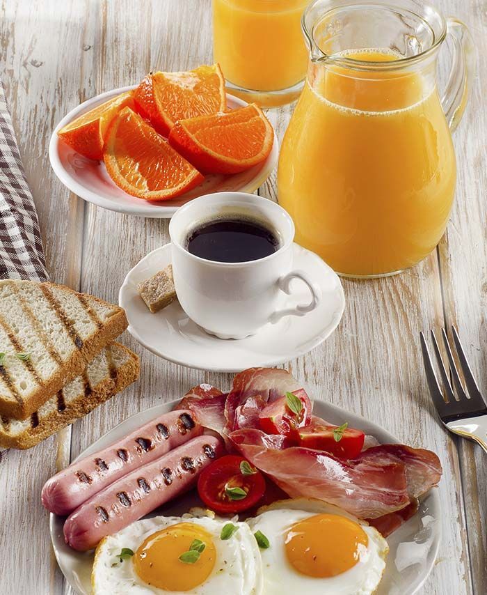 Una mesa de madera cubierta con platos de comida que incluían huevos, tocino y naranjas.