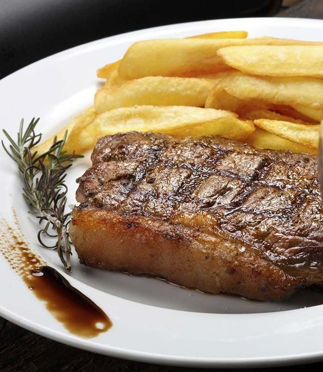 Un plato blanco cubierto con un bistec y papas fritas