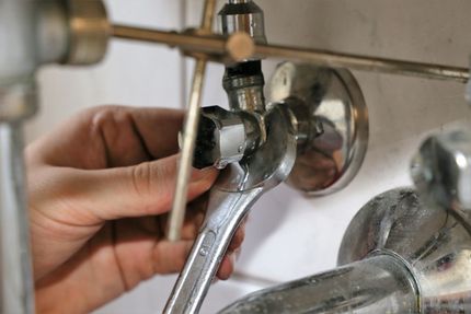 Klempner verbindet graue Rohre unter einem Waschbecken. Zu sehen sind Hände, verschiedene Rohre und flexible Wasserleitungen.