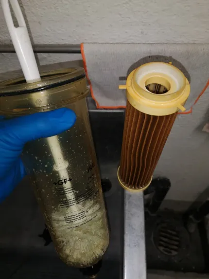 Klempner verbindet graue Rohre unter einem Waschbecken. Zu sehen sind Hände, verschiedene Rohre und flexible Wasserleitungen.
