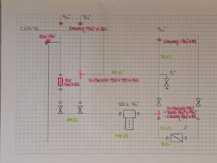 Vier Anodenstäbe eines Warmwasserbereiters, zwei neue und silberne, zwei alte und korrodierte, liegen auf einem Betonboden in der Nähe einer Wand.