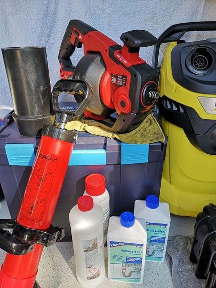 Eine Hand dreht ein Ventil mit gelbem Griff an einem Kupferrohr, das wahrscheinlich den Wasserfluss regelt und vor einer weißen Wand steht.