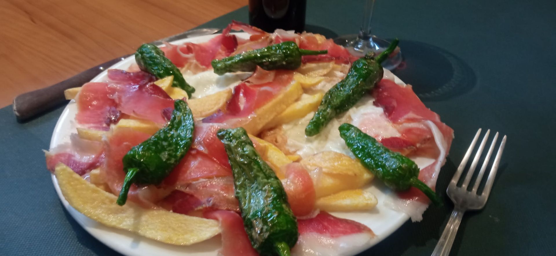 Plato de comida: jamón, pimientos y patatas fritas en un plato blanco, con un tenedor sobre un tapete verde.