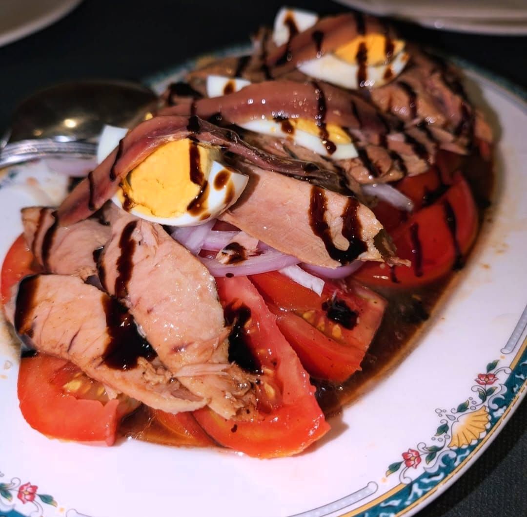 Ensalada de atún con tomates, cebollas, huevos y glaseado balsámico en un plato decorativo.