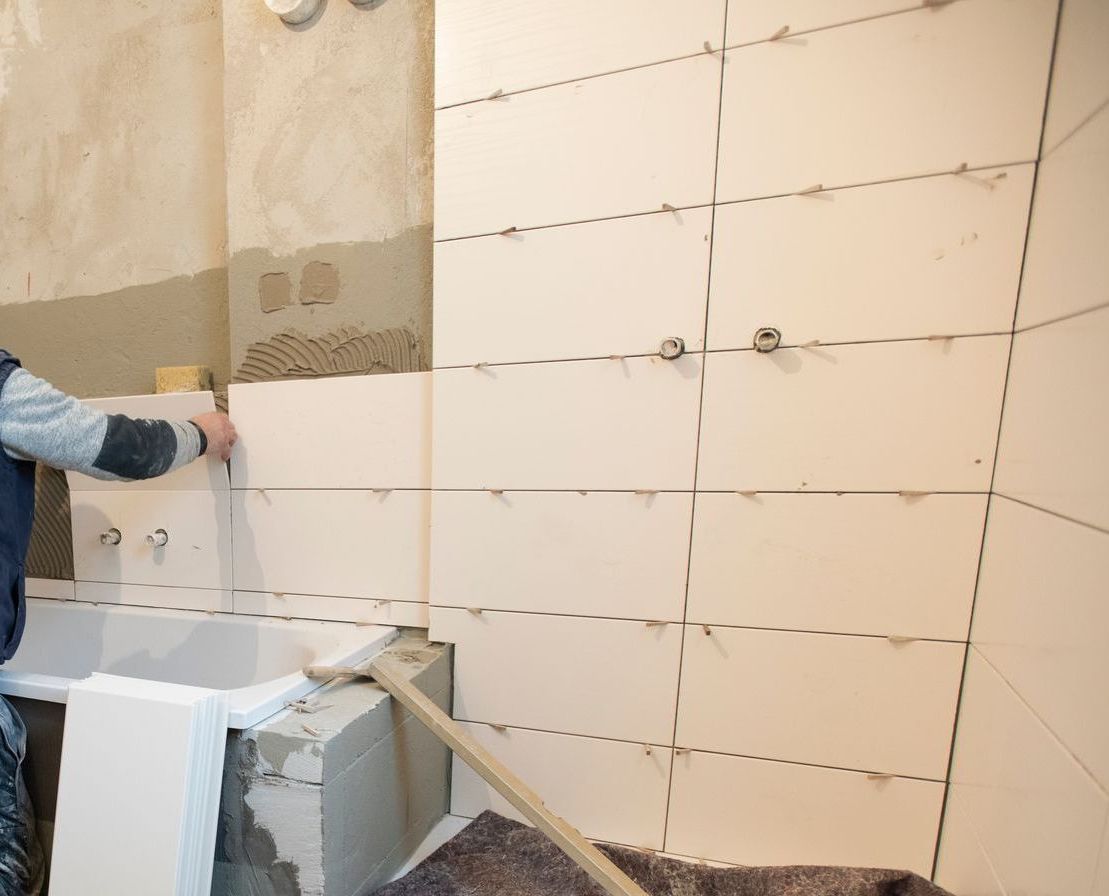 Person, die eine Badezimmerwand mit weißen rechteckigen Fliesen fliest.