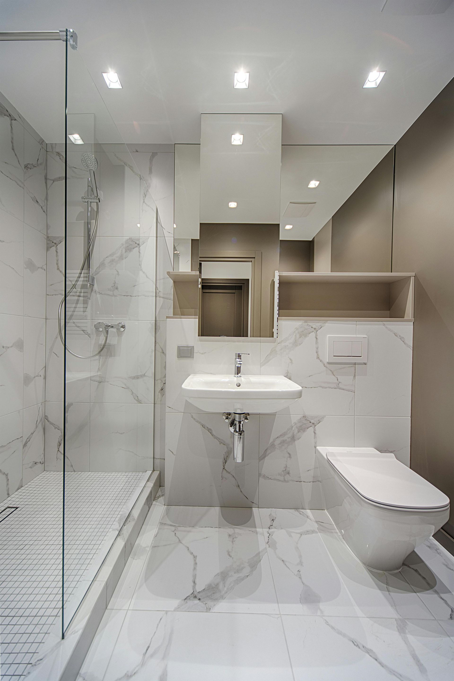 Modernes Badezimmer mit marmorähnlichen Fliesen, Glasdusche, weißen Armaturen und einem eingebauten Spiegel über dem Waschbecken.