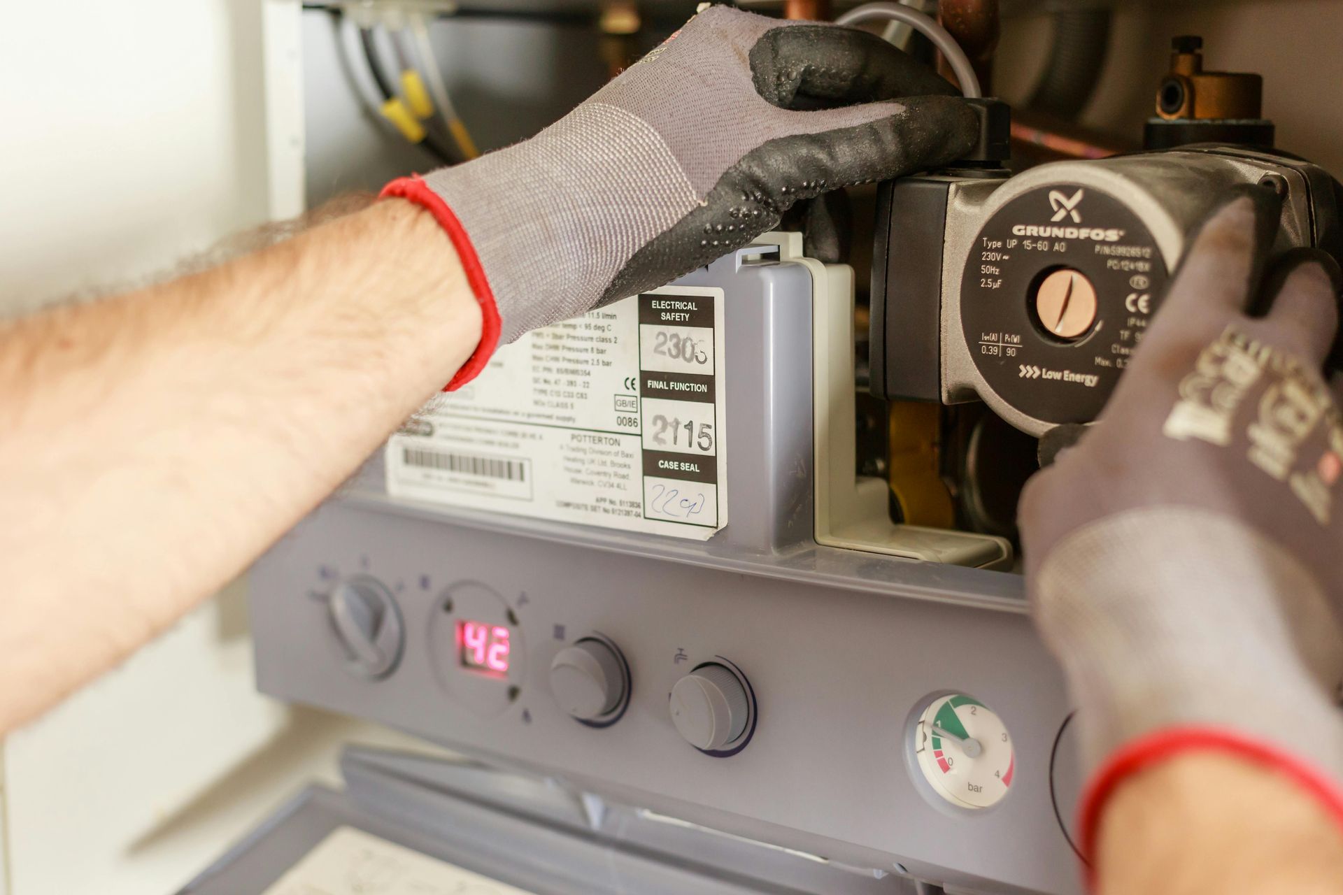 Hände in Arbeitshandschuhen reparieren einen Kessel, wobei der Schwerpunkt auf einer Pumpenkomponente liegt.
