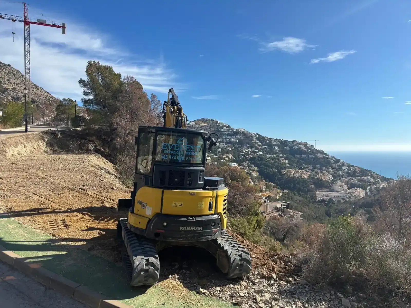 Excavadora amarilla demoliendo un edificio, levantando polvo bajo un cielo azul.