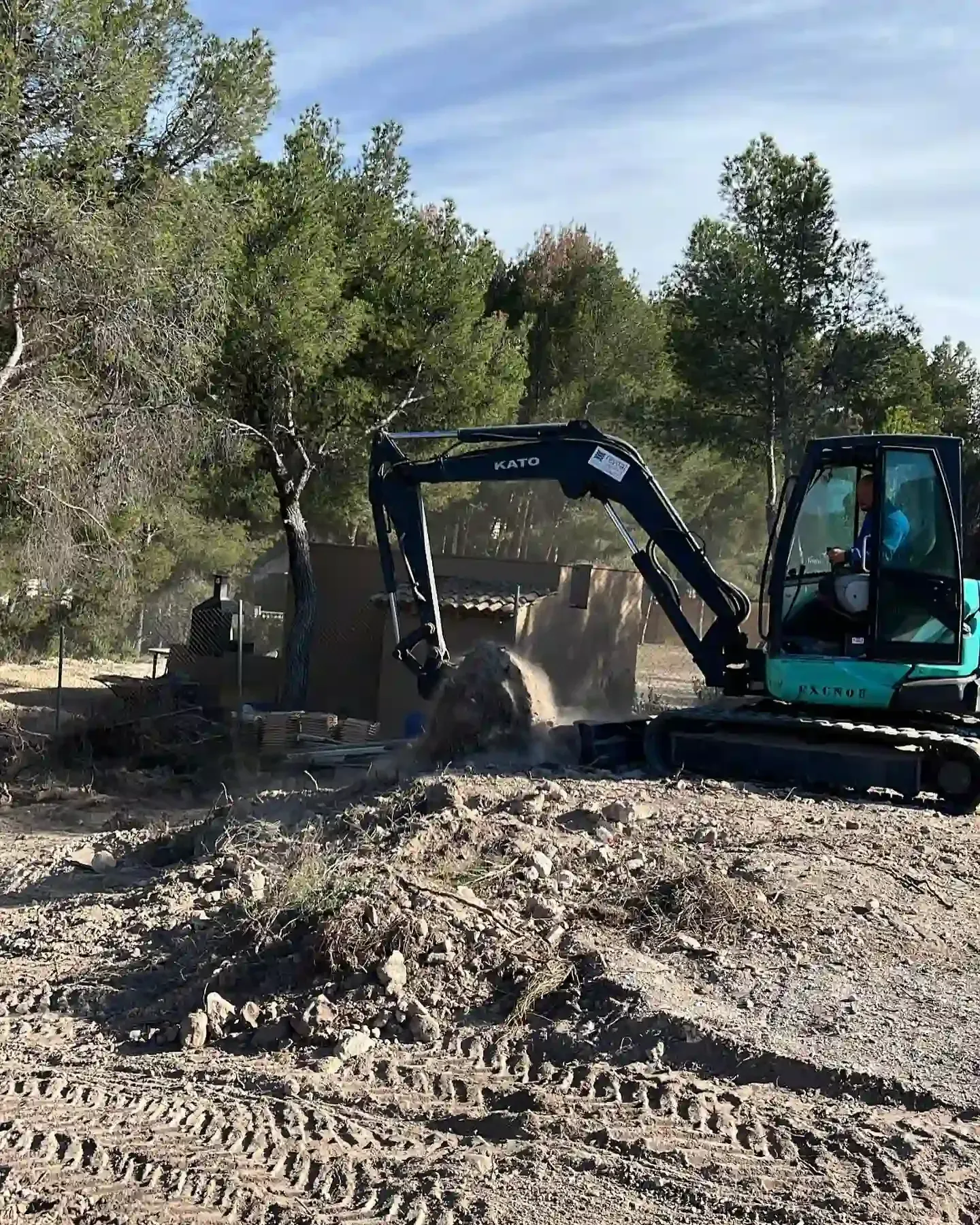 Excavadora amarilla cargando escombros de demolición en la plataforma de un camión rojo.