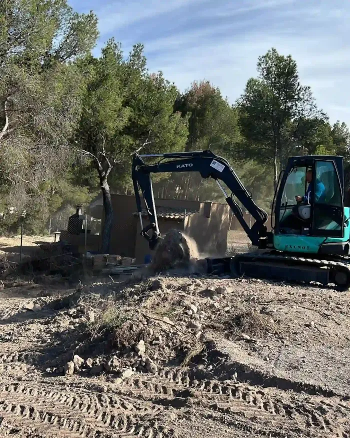 Excavadora amarilla cargando escombros de demolición en la plataforma de un camión rojo.
