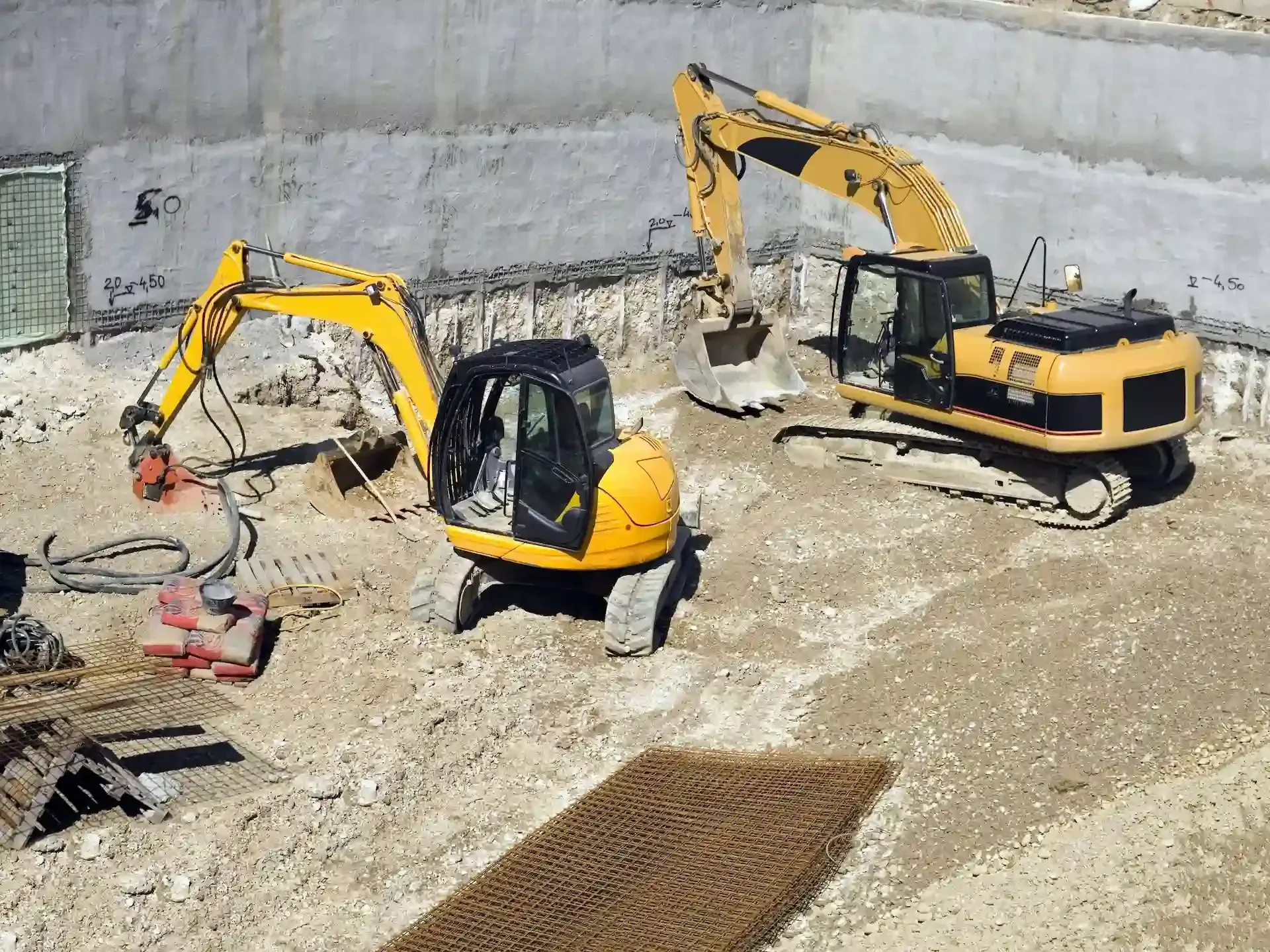 Dos excavadoras amarillas en un pozo de construcción, trabajando en una estructura de hormigón.