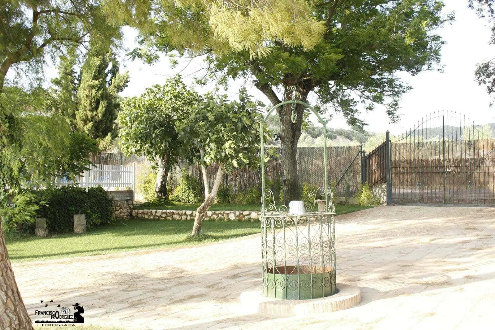 Un pozo en un patio con césped, rodeado de árboles y con una entrada cerrada.