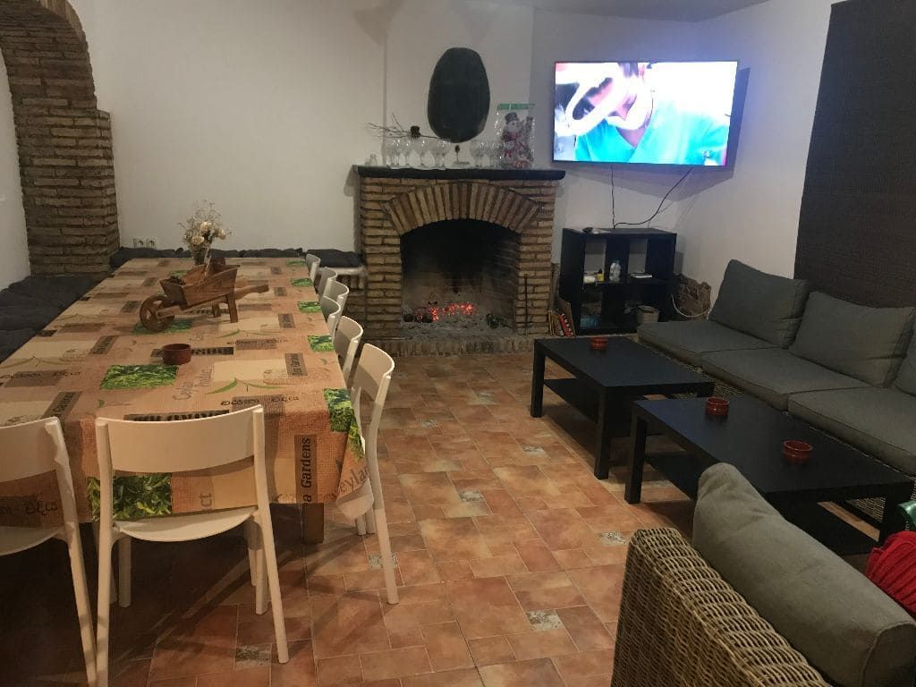 Una sala de estar con chimenea, mesa larga, sillas, sofá, TV y mesas negras.