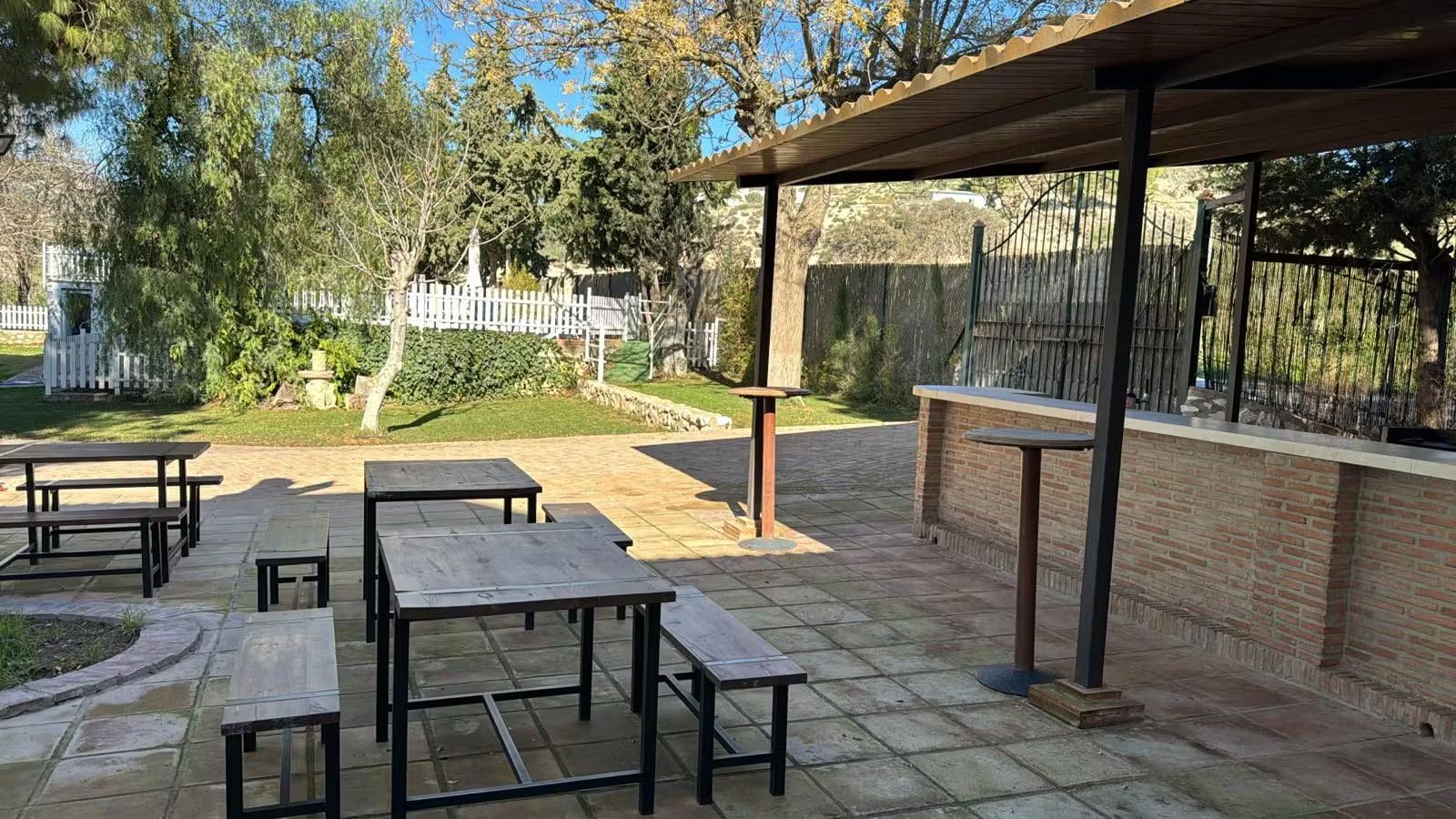 Patio exterior con mesas y bancos de madera, bajo un dosel de sombra.