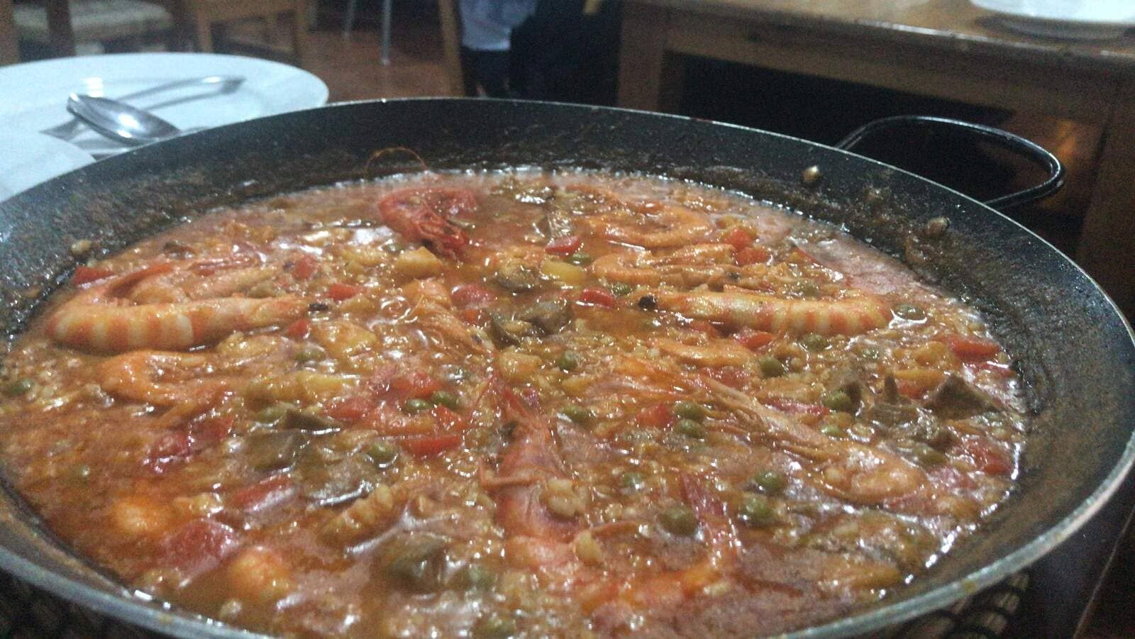 Paella con camarones en una sartén grande y oscura sobre una mesa, lista para ser servida.