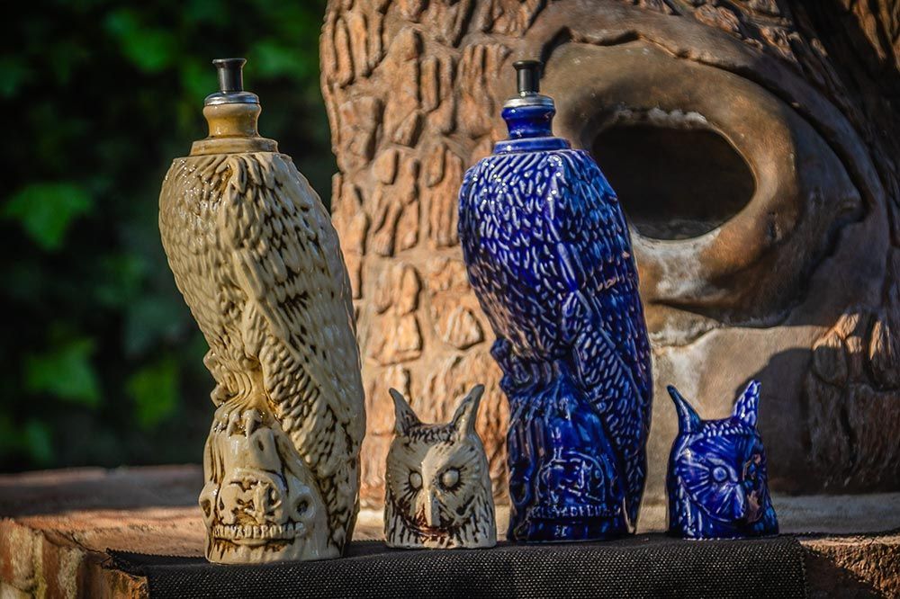 Dos botellas de cerámica con forma de búho y dos figuritas de búho más pequeñas se encuentran sobre una superficie de piedra al aire libre.