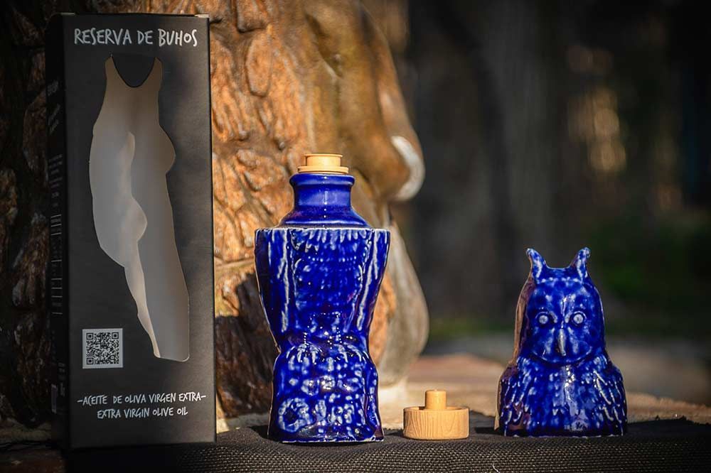 Una caja negra junto a una botella de cerámica azul con forma de gato, con su tapa azul a juego con forma de cabeza de gato cerca.