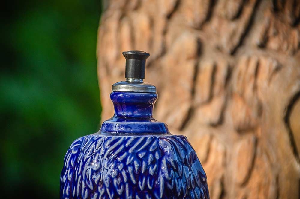 Un objeto de cerámica azul con textura, posiblemente una lámpara o un difusor, se encuentra sobre un fondo de madera tallada y difuminada.