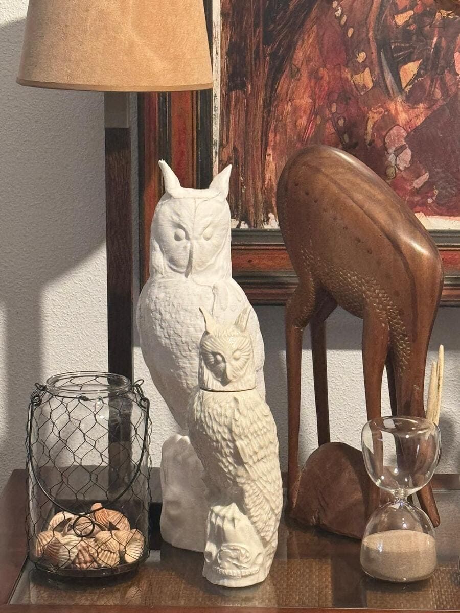 Una estatua de un búho sentado en una mesa junto a una lámpara.