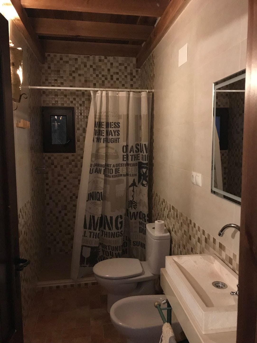 Baño con inodoro, bidet, lavabo, cortina de ducha y paredes de mosaico.