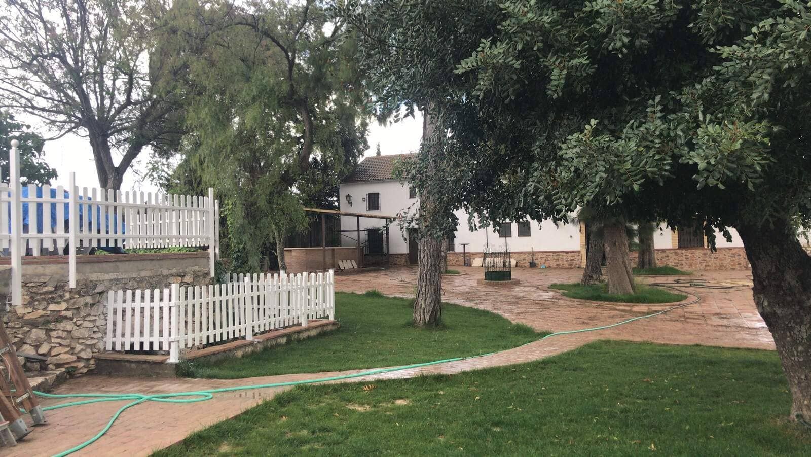 Un patio verde con una cerca blanca, árboles y un edificio blanco al fondo.