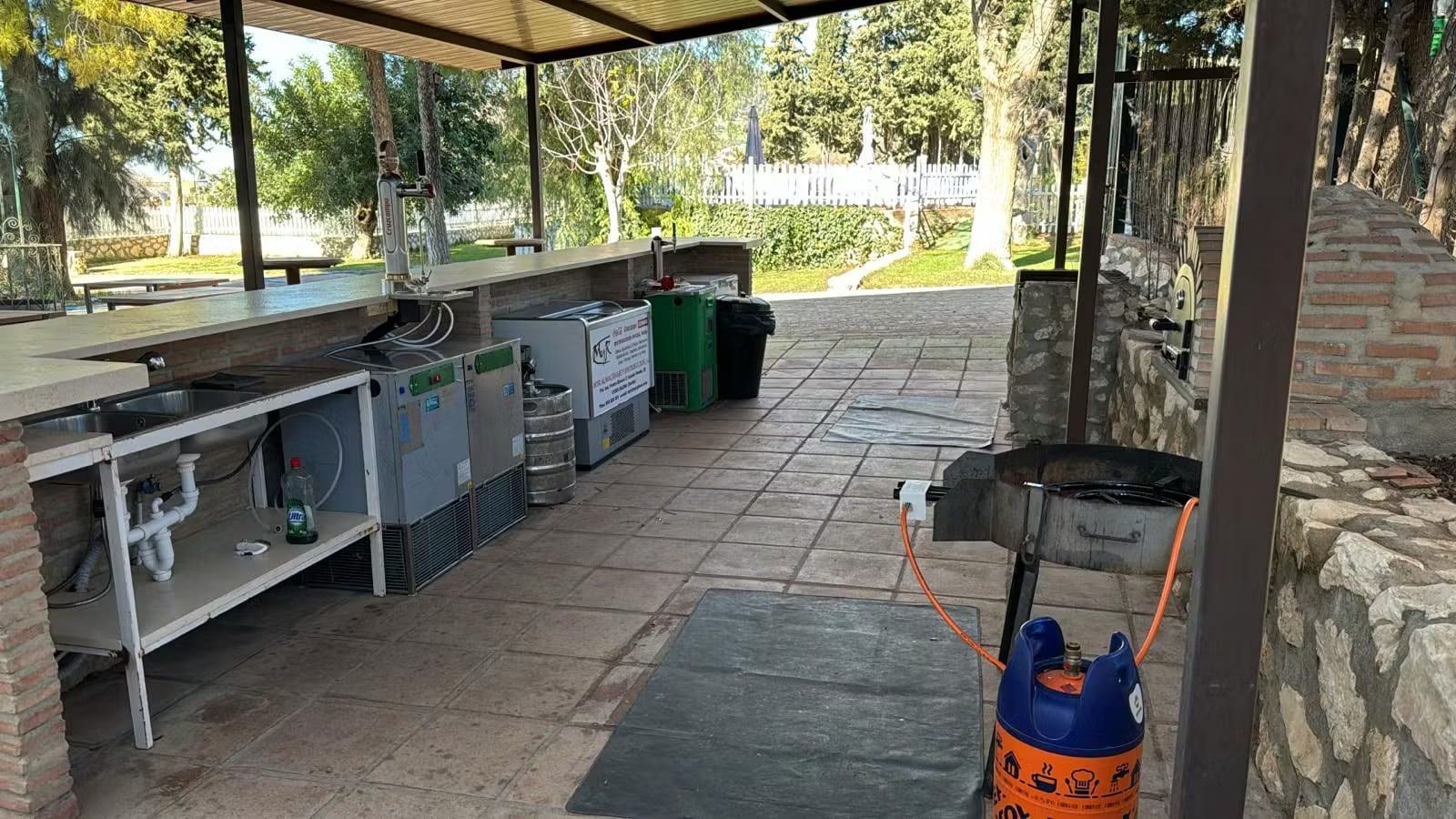 Cocina exterior con encimera, electrodomésticos y parrilla bajo zona techada.