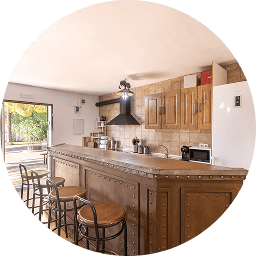 Cocina con barra y taburetes, gabinetes, electrodomésticos y puerta abierta al exterior.