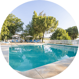 Piscina rodeada de árboles y una valla blanca bajo un cielo azul.
