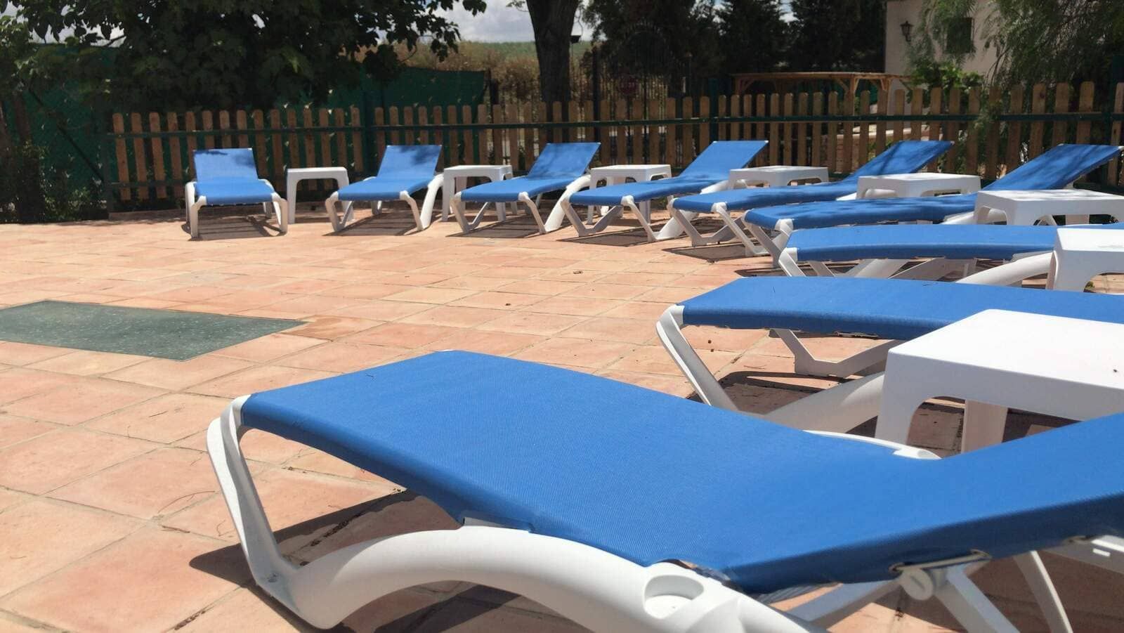 Sillones con cojines azules y armazones blancos se encuentran en un patio de ladrillo. Cerca hay mesas blancas.