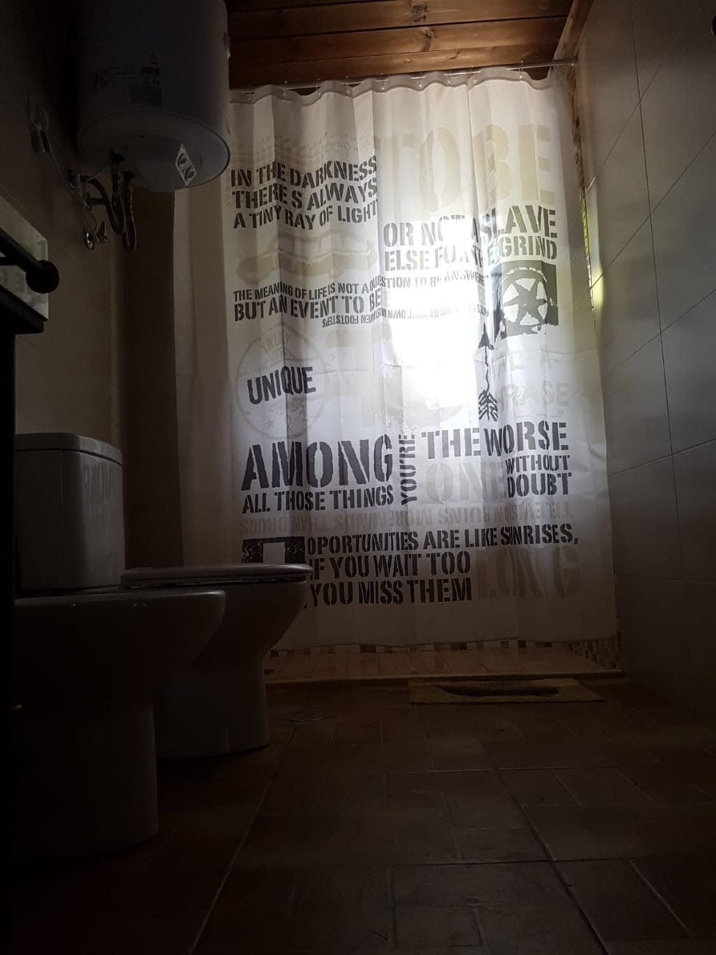 Baño con inodoro, cortina de ducha con texto y calentador de agua.