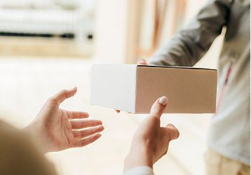 Persona entregando un paquete a otra persona; con ambas manos extendidas hacia una caja de cartón.