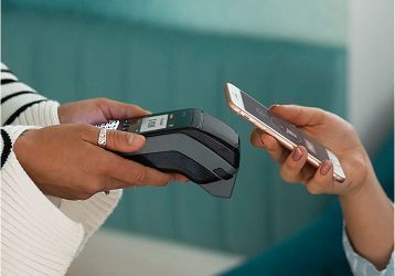 Persona que utiliza un teléfono inteligente para realizar un pago sin contacto en un lector de tarjetas.