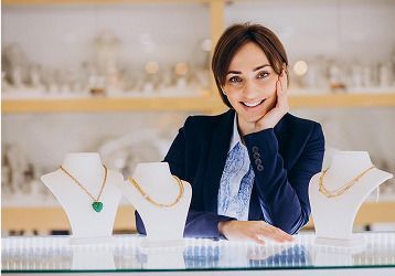 Joyero sonríe, apoyado en una vitrina con collares en maniquíes. Entorno de joyería.