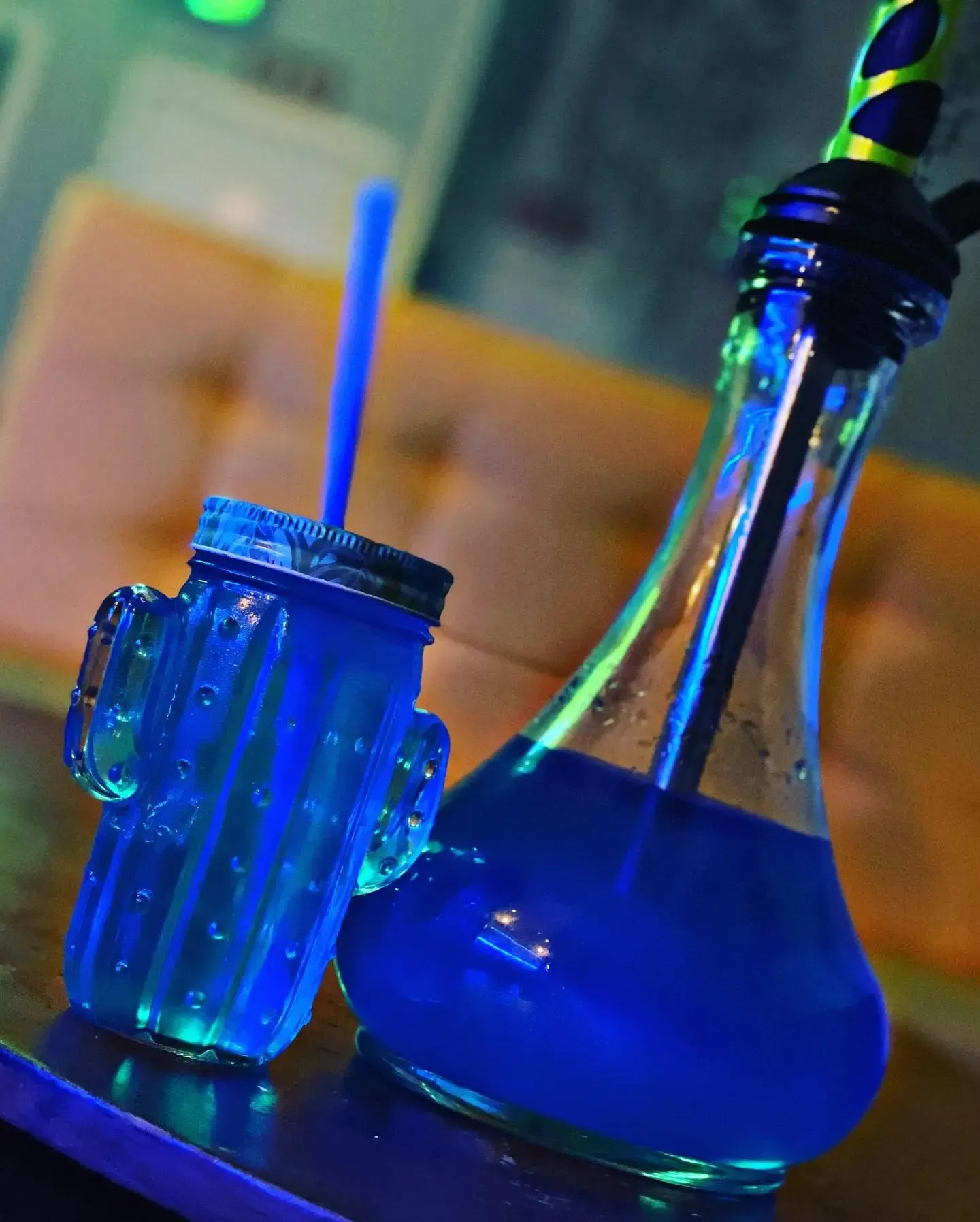 Cachimba azul y vaso en forma de cactus con líquido azul y pajita, sobre una mesa.
