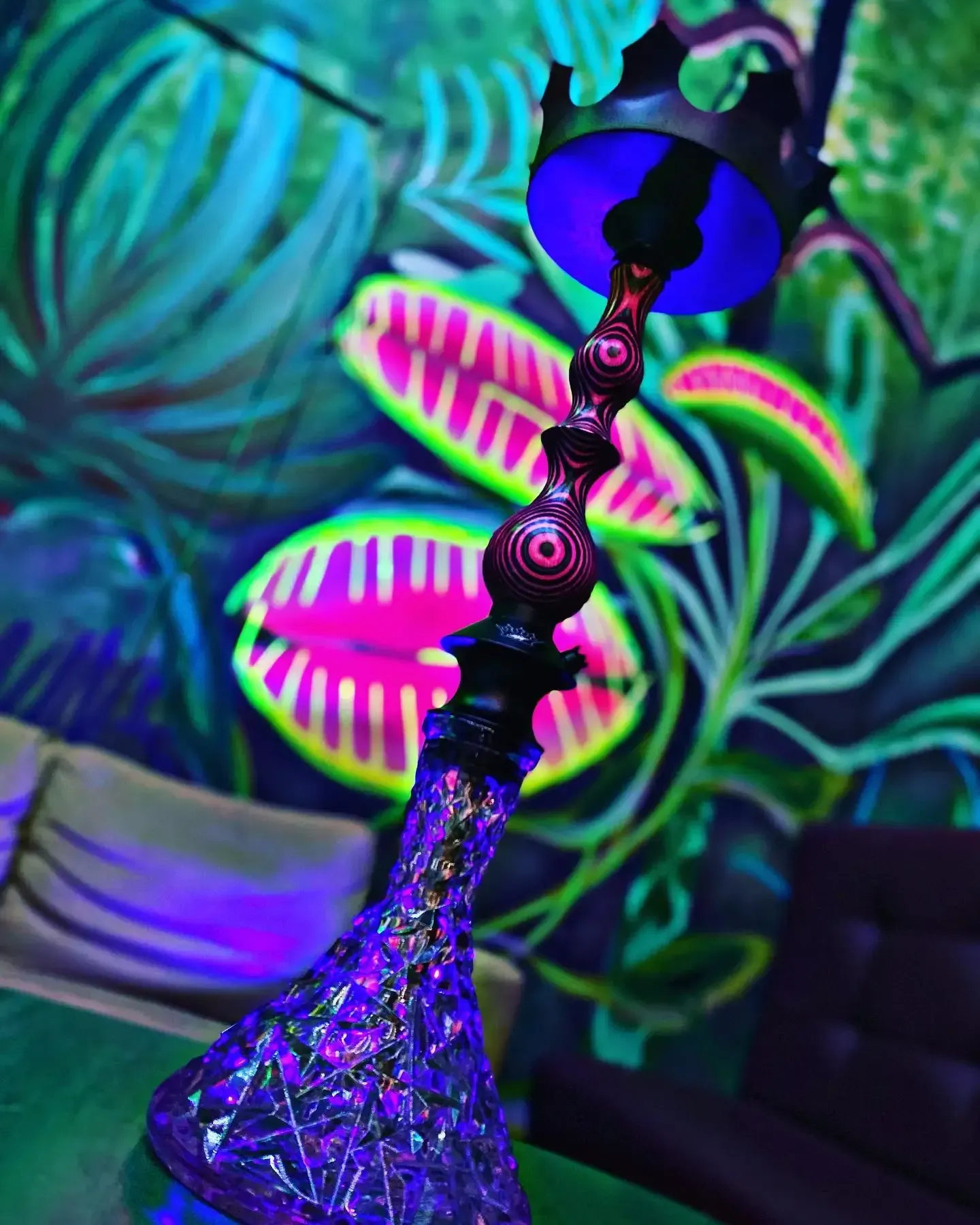 Cachimba con brillo violeta sobre un mural de plantas grandes y coloridas.