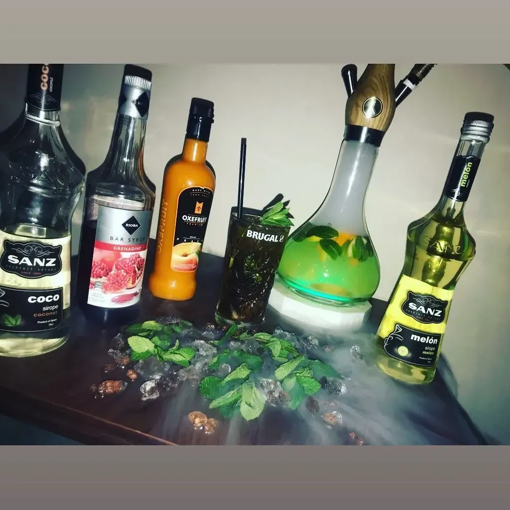 Configuración de cachimba con botellas, bebida, menta y vapor.