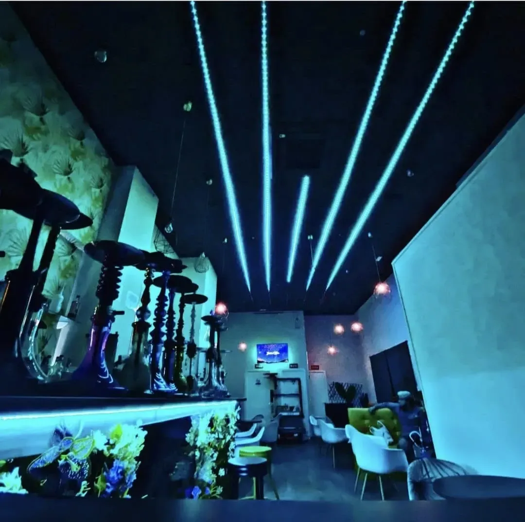Interior de un salón de narguile con luces de techo azules y una fila de narguiles.